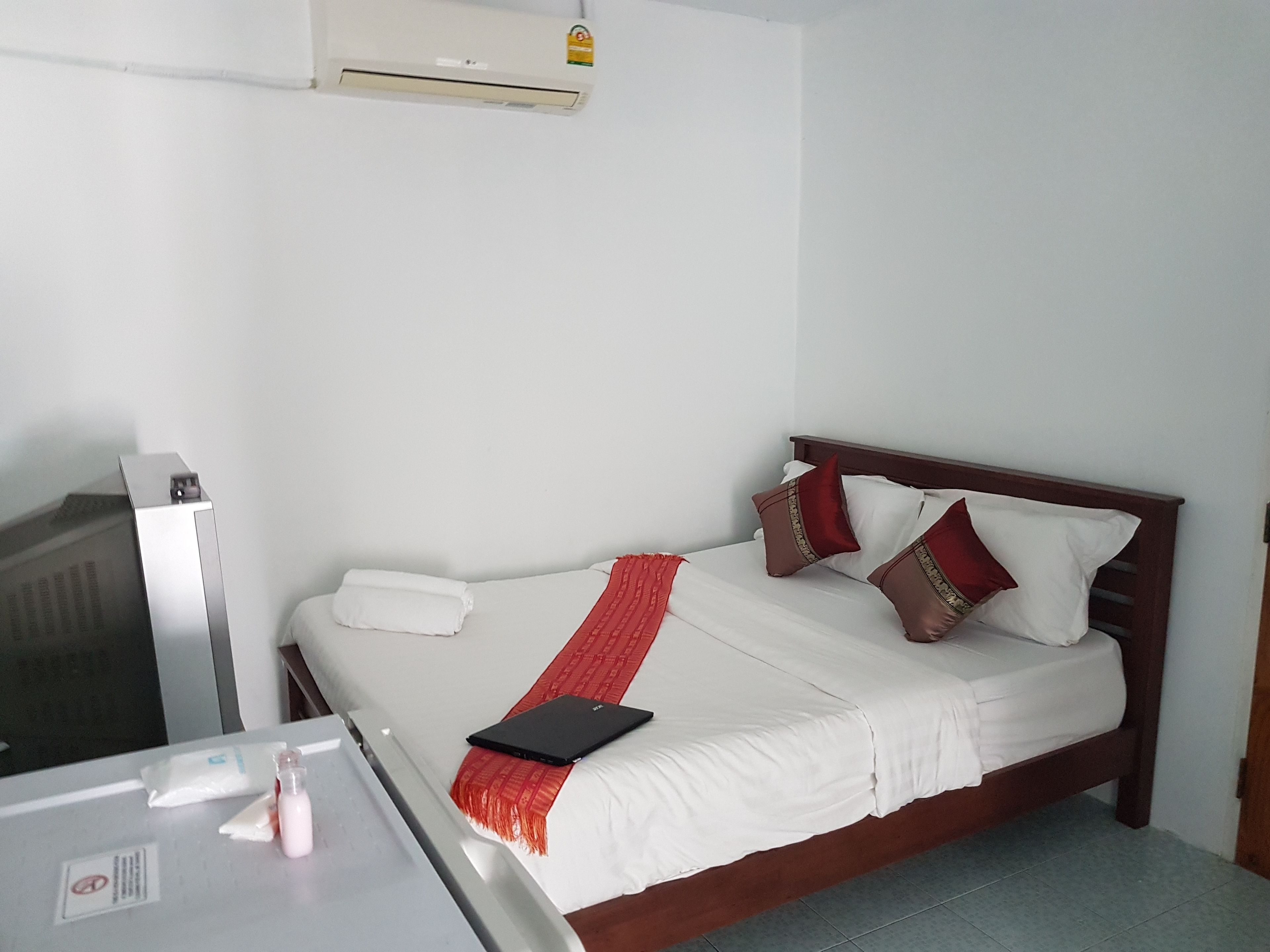 A hotel room with a bed, a bedside table, a TV, and an air conditioner.