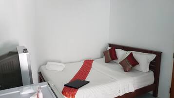 A hotel room with a bed, a bedside table, a TV, and an air conditioner.