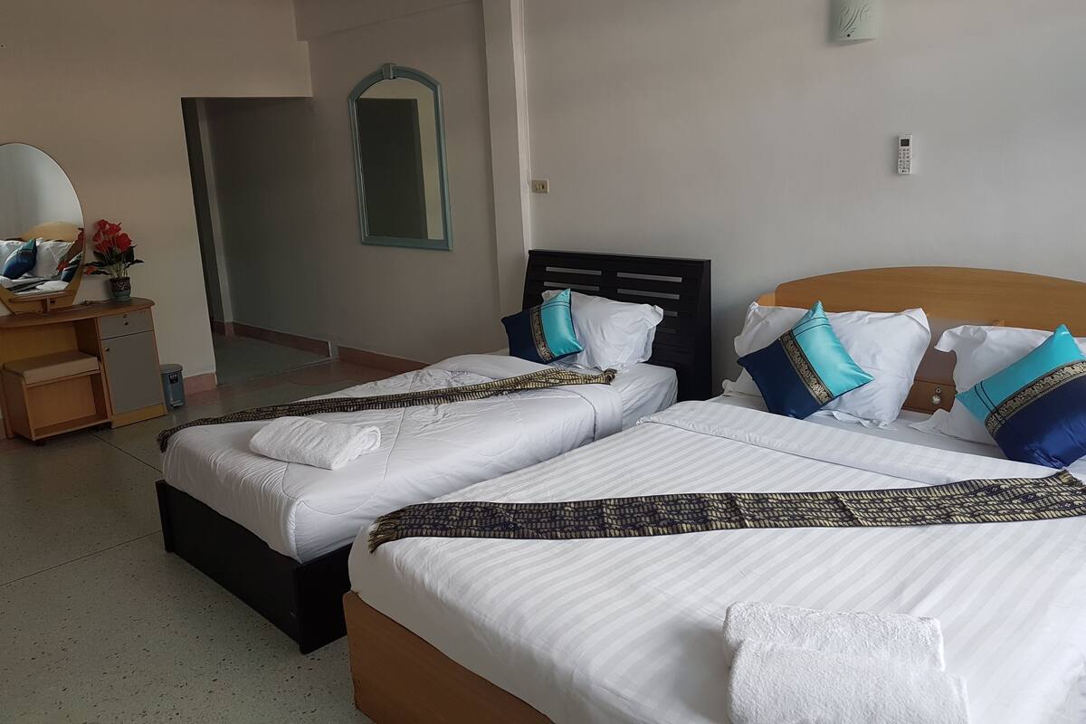 Quarto de hotel com duas camas, uma mesa de cabeceira de madeira, um espelho e um ponto de luz fixado na parede.