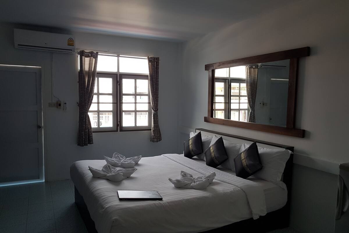 Quarto de hotel com cama, janela com cortinas, espelho fixado na parede e termostato.