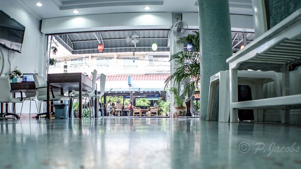 A spacious lobby with a high ceiling, multiple seating areas, and a large window offering a view of the outside. - Chaam Guesthouse (Cha-am)