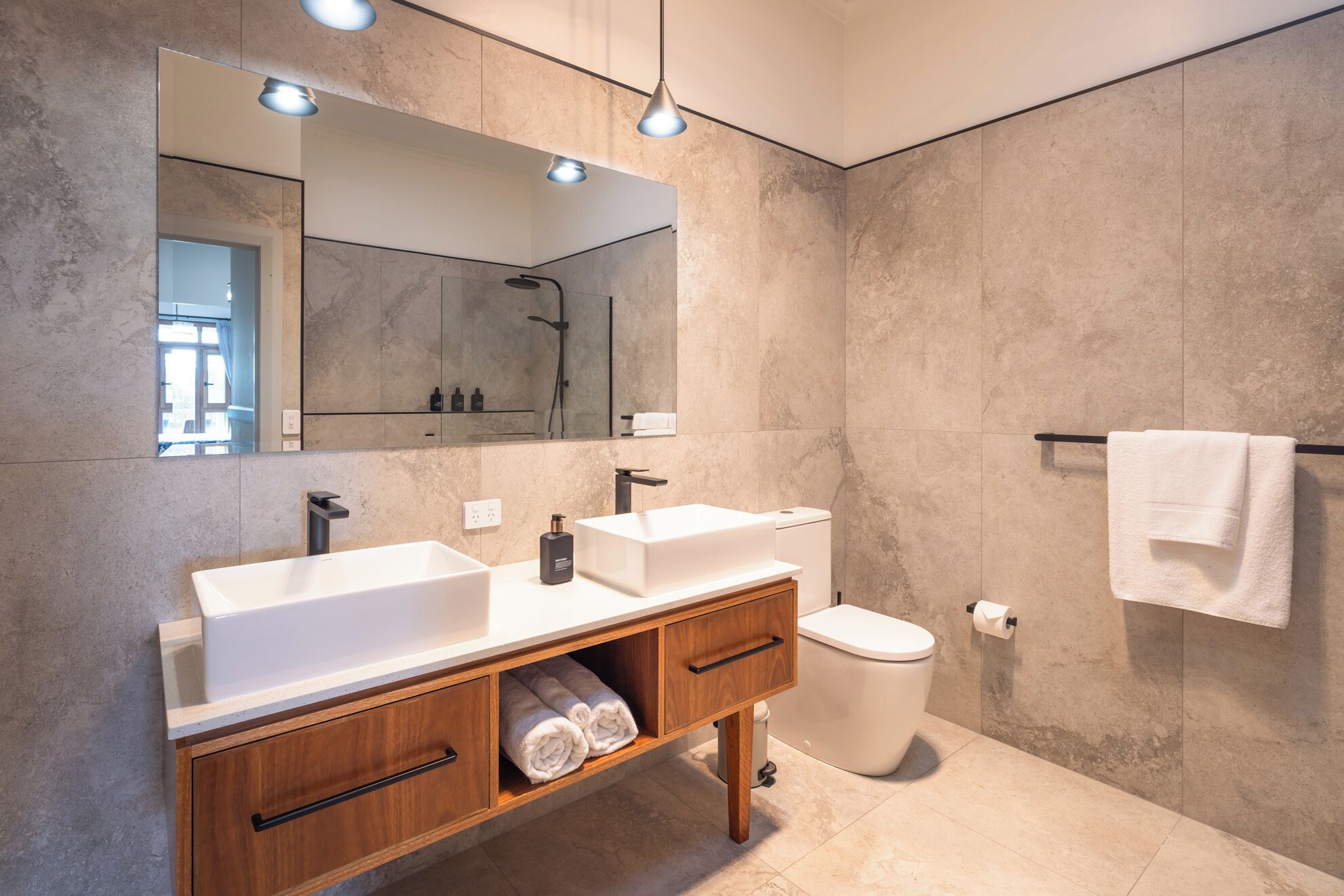Un bagno moderno con due lavandini, un water e uno specchio grande.