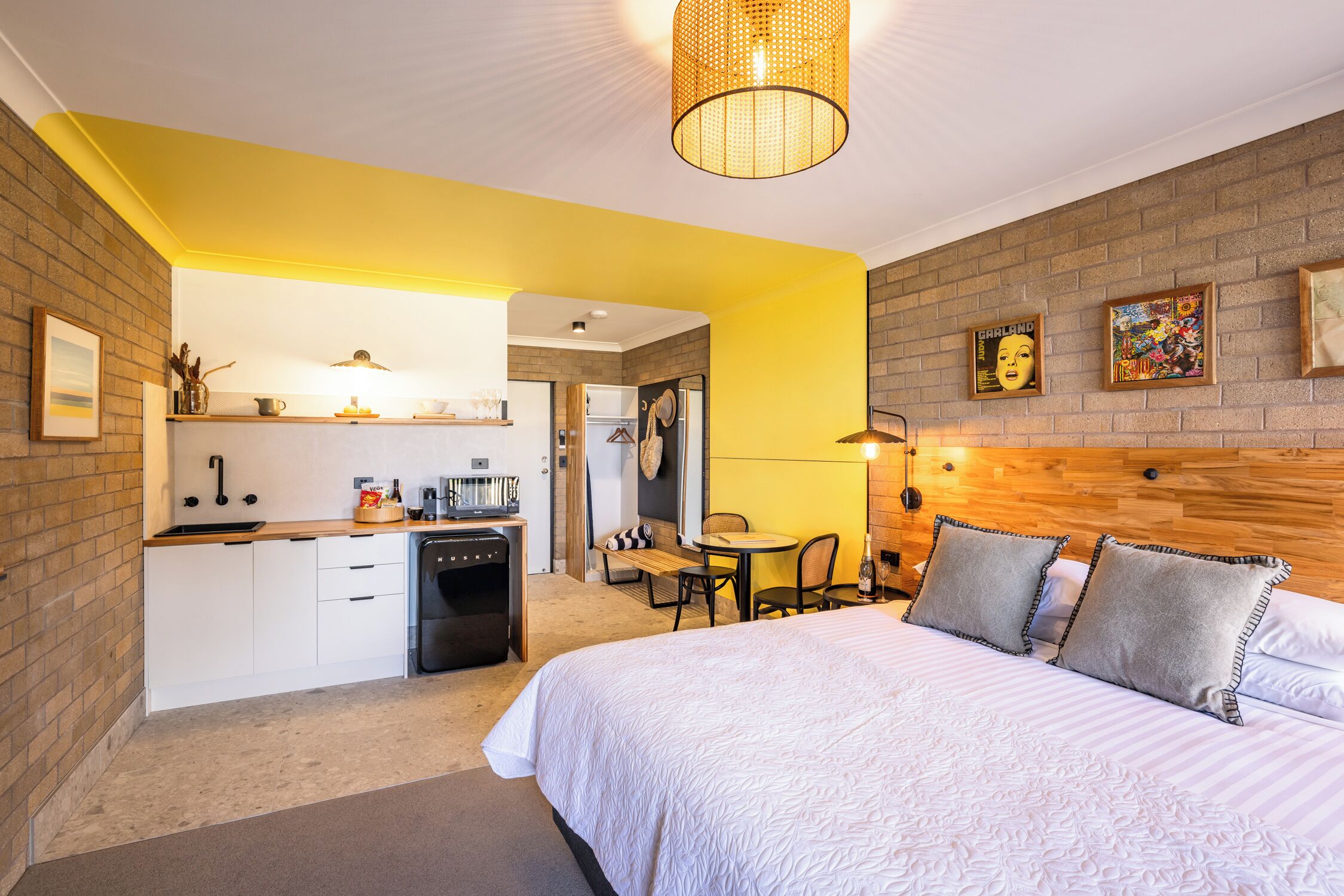 A hotel room with a bed, a small kitchenette, a dining area, and a brick wall.