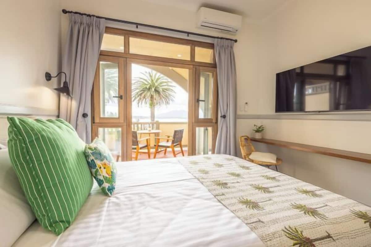 Una habitación de hotel con una cama, una ventana con cortinas, una mesita pequeña y una silla.