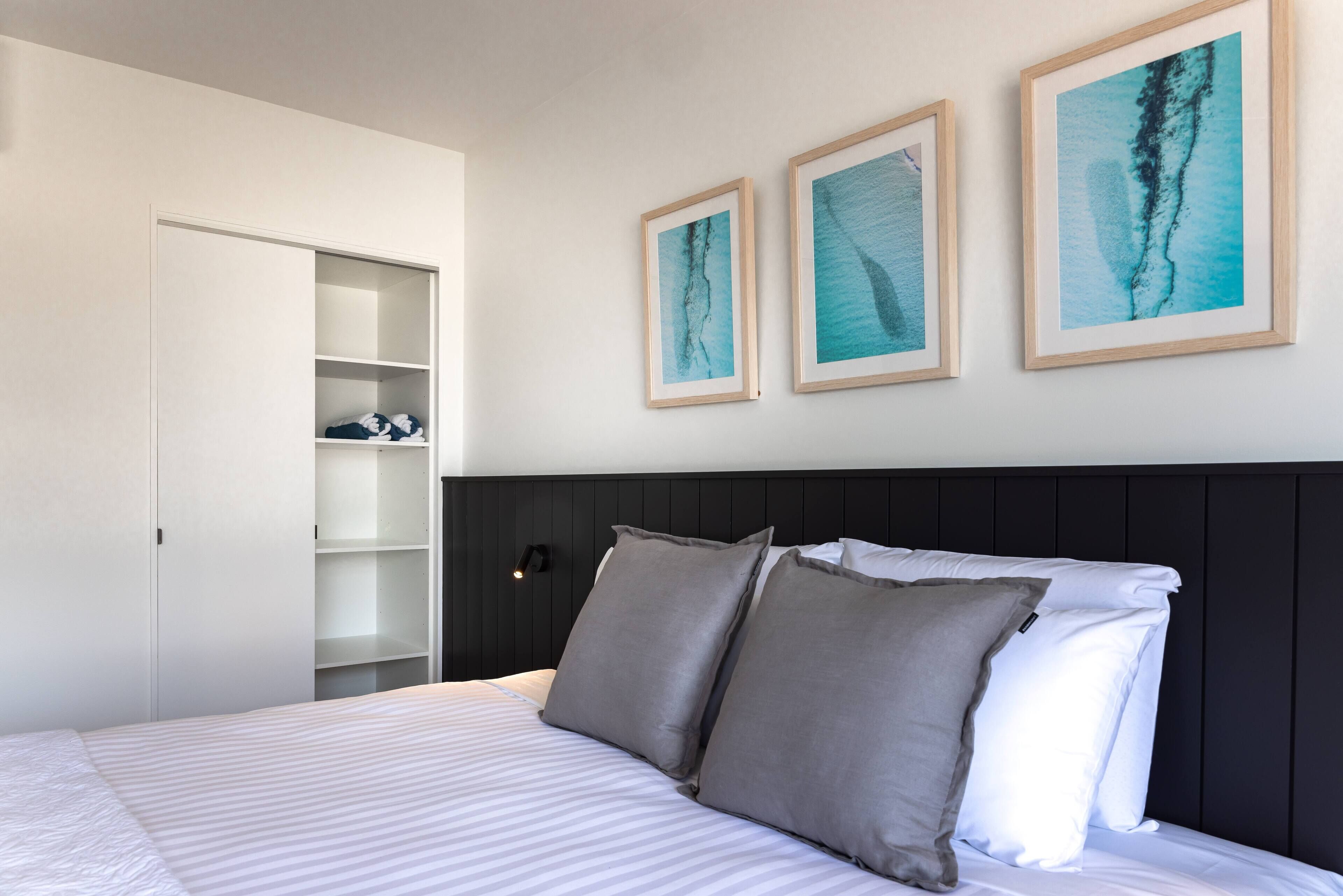 Ein Hotelzimmer mit einem Bett, einem Kleiderschrank und drei gerahmten Kunstwerken an der Wand.