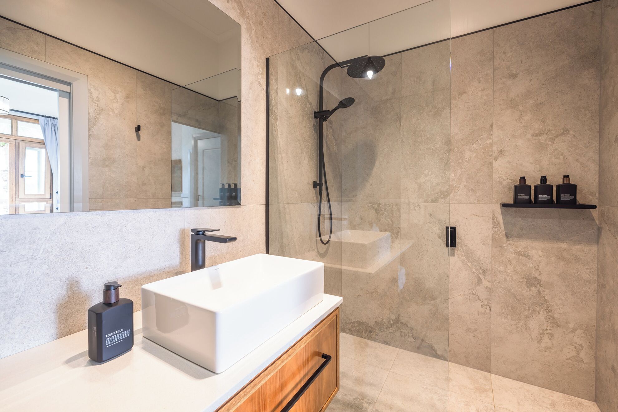 A modern bathroom with a white sink, a handheld showerhead, and a mirror.