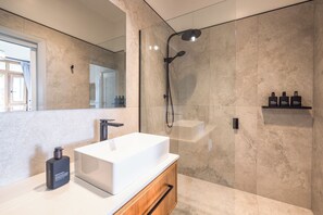 Un baño moderno con un lavamanos blanco, un cabezal de ducha manual y un espejo.