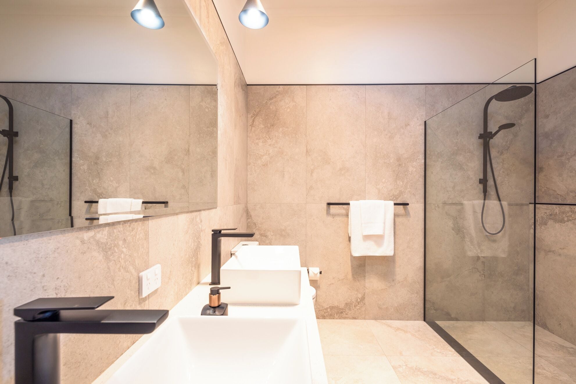 A modern bathroom with a large mirror, a white sink, a handheld showerhead, and a towel rack.