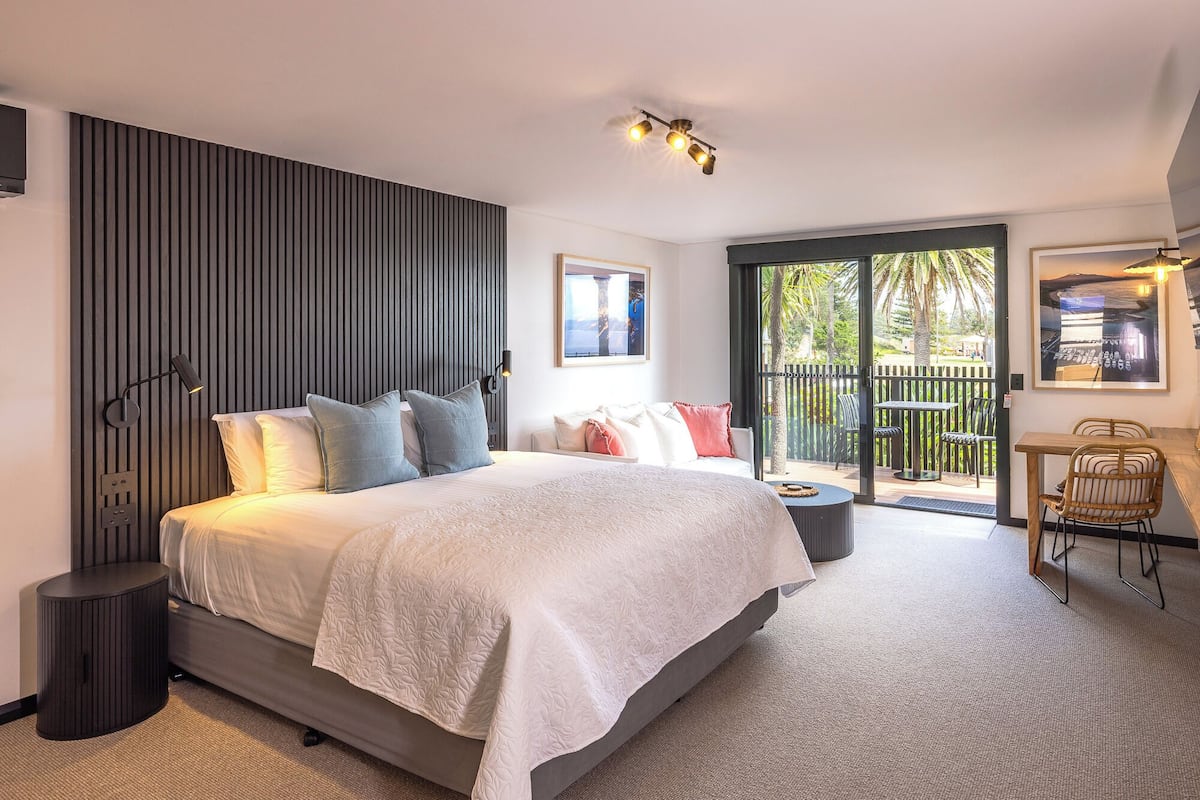 Un dormitorio moderno con una cama grande, una mesita de noche, una lámpara de pared y vistas al exterior a través de una puerta corredera.