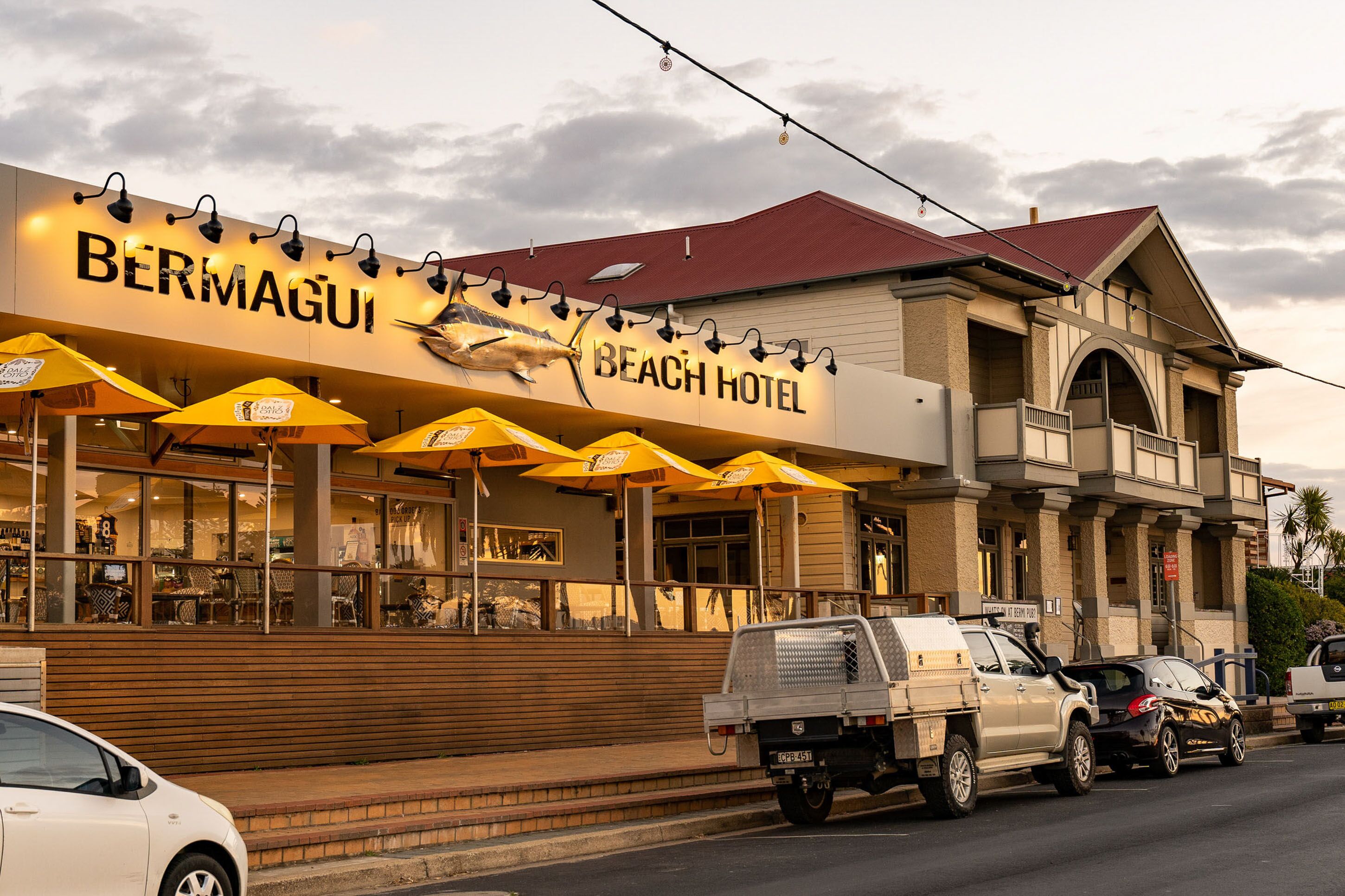 A beach hotel with outdoor seating and a sign displaying the name.