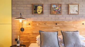 Habitación de hotel con pared de ladrillo, cabecero de madera y una mesita con una botella y vasos.