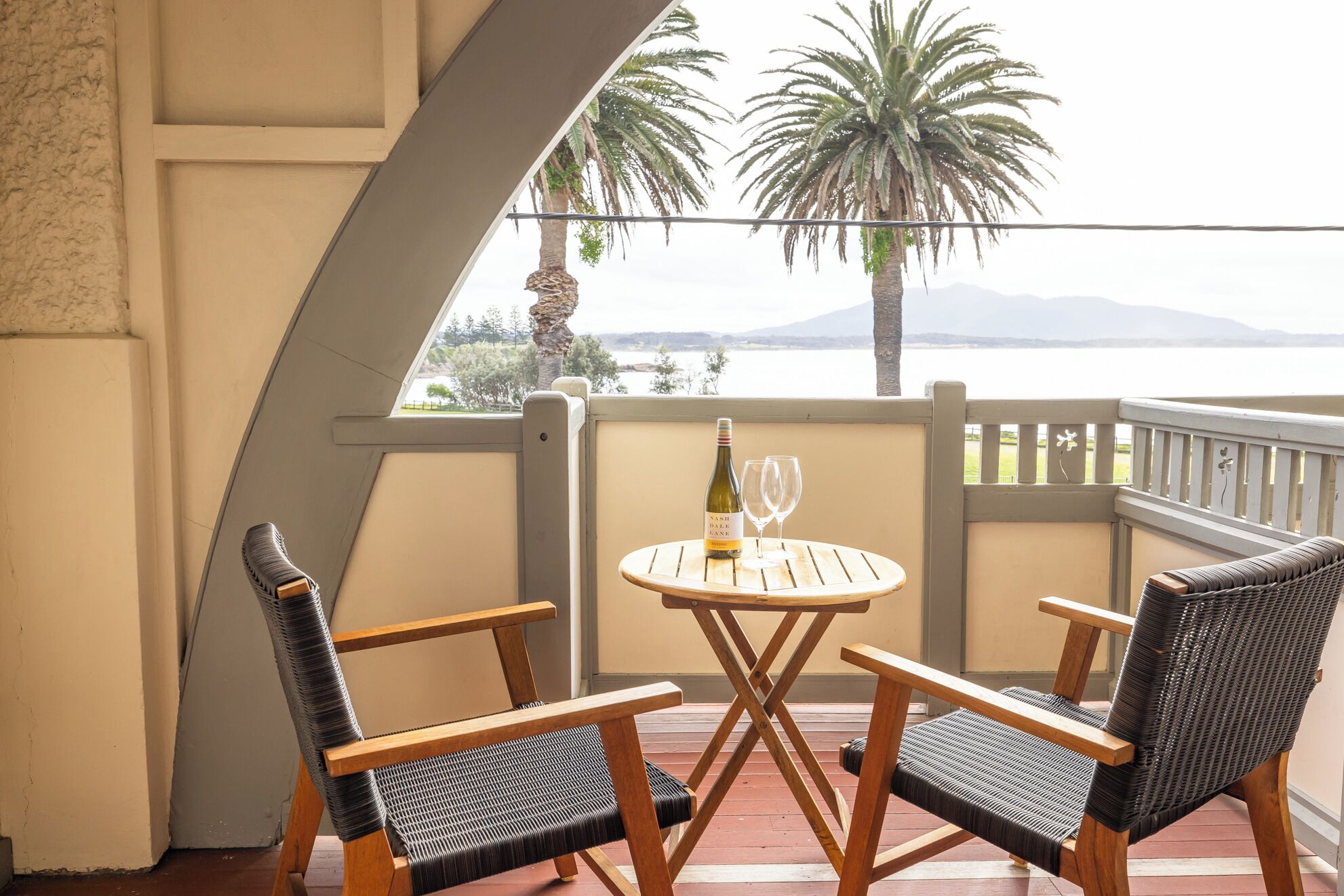 A balcony with two wicker chairs, a small round table, and a bottle of wine.