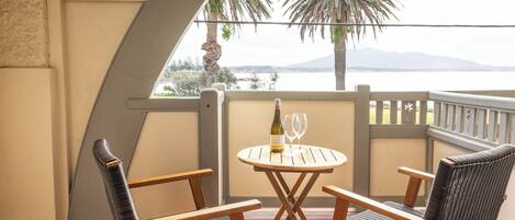 A balcony with two wicker chairs, a small round table, and a bottle of wine.