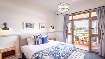A bedroom with a large bed, a bench, a chandelier, and a view of the outdoors through a glass door.