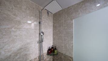 A shower with a square head, a handheld showerhead, and a glass shelf with three bottles.