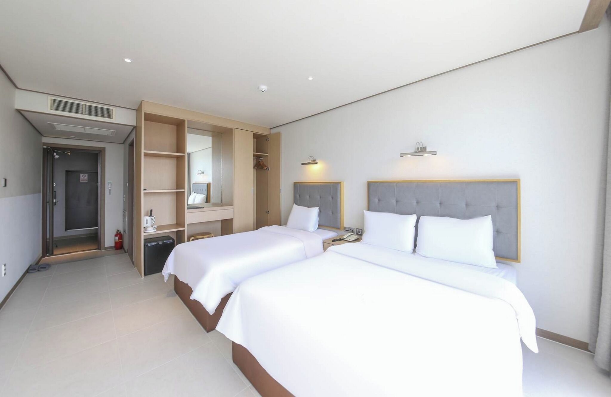A hotel room with two beds, a wardrobe, a mirror, a bedside table, and a small desk.