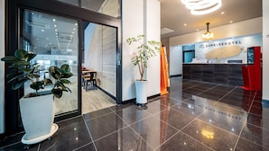 Un moderno vestíbulo de hotel con un mostrador de recepción, una planta grande en maceta y vistas al salón de comidas.