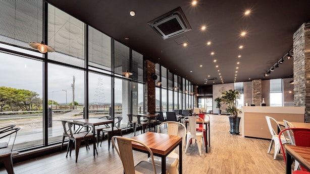 Un restaurante moderno con amplios ventanales, mesas y sillas de madera.