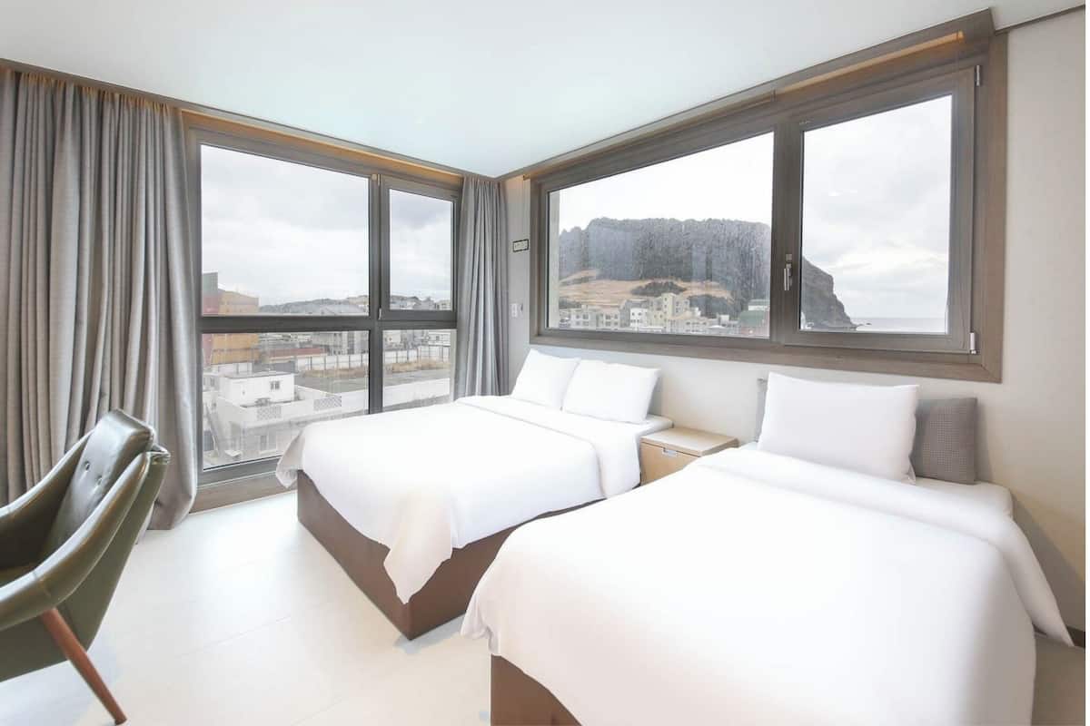 Een hotelkamer met twee bedden, een stoel en grote ramen met uitzicht op de stad.