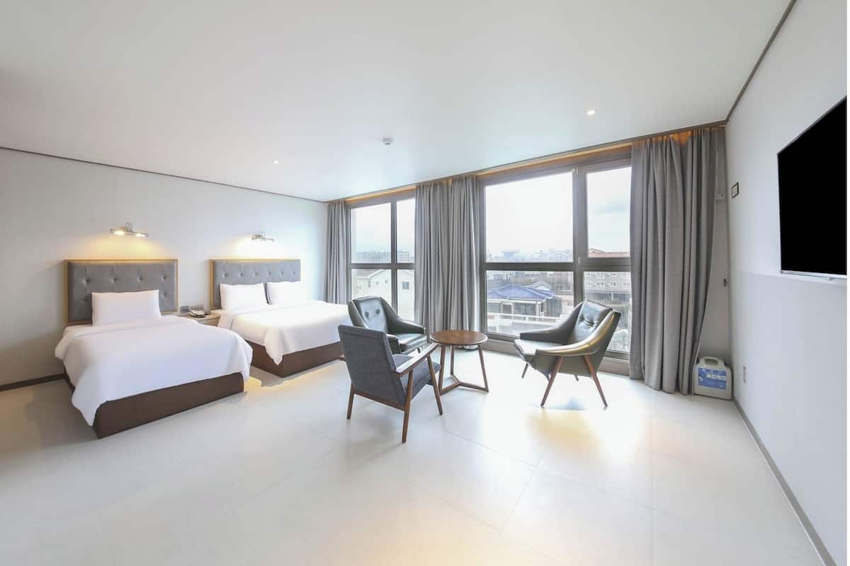 Hotelkamer met twee bedden, een bureau, twee stoelen, een groot raam met gordijnen en een flatscreen-televisie.