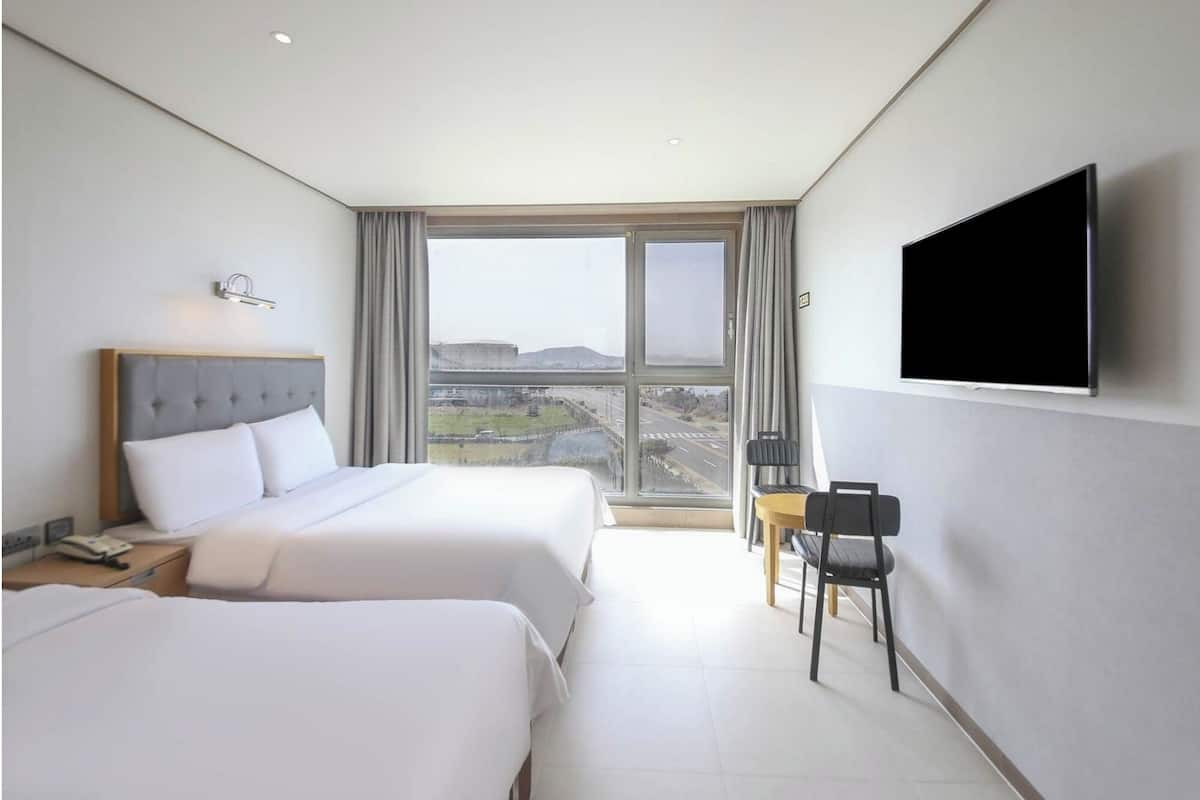 Een hotelkamer met twee bedden, een televisie, een bureau met telefoon en uitzicht op een stadsbeeld.