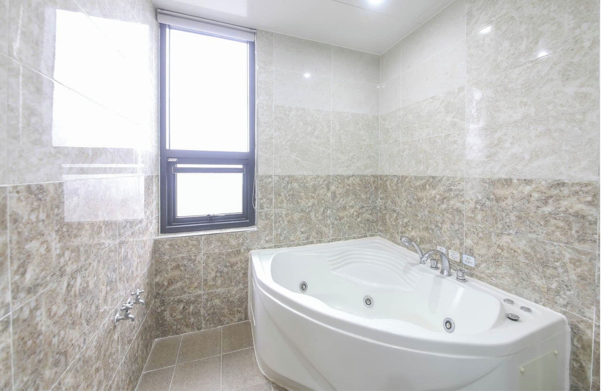 Un baño con una bañera grande, una ventana y paredes de mármol.