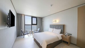 Habitación de hotel con cama, mesita de noche, televisión y vista al mar.