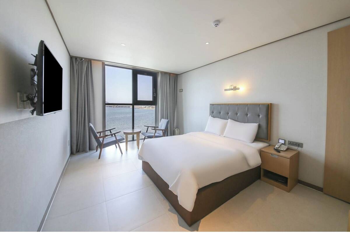 Een hotelkamer met een bed, nachtkastje, televisie en uitzicht op zee.