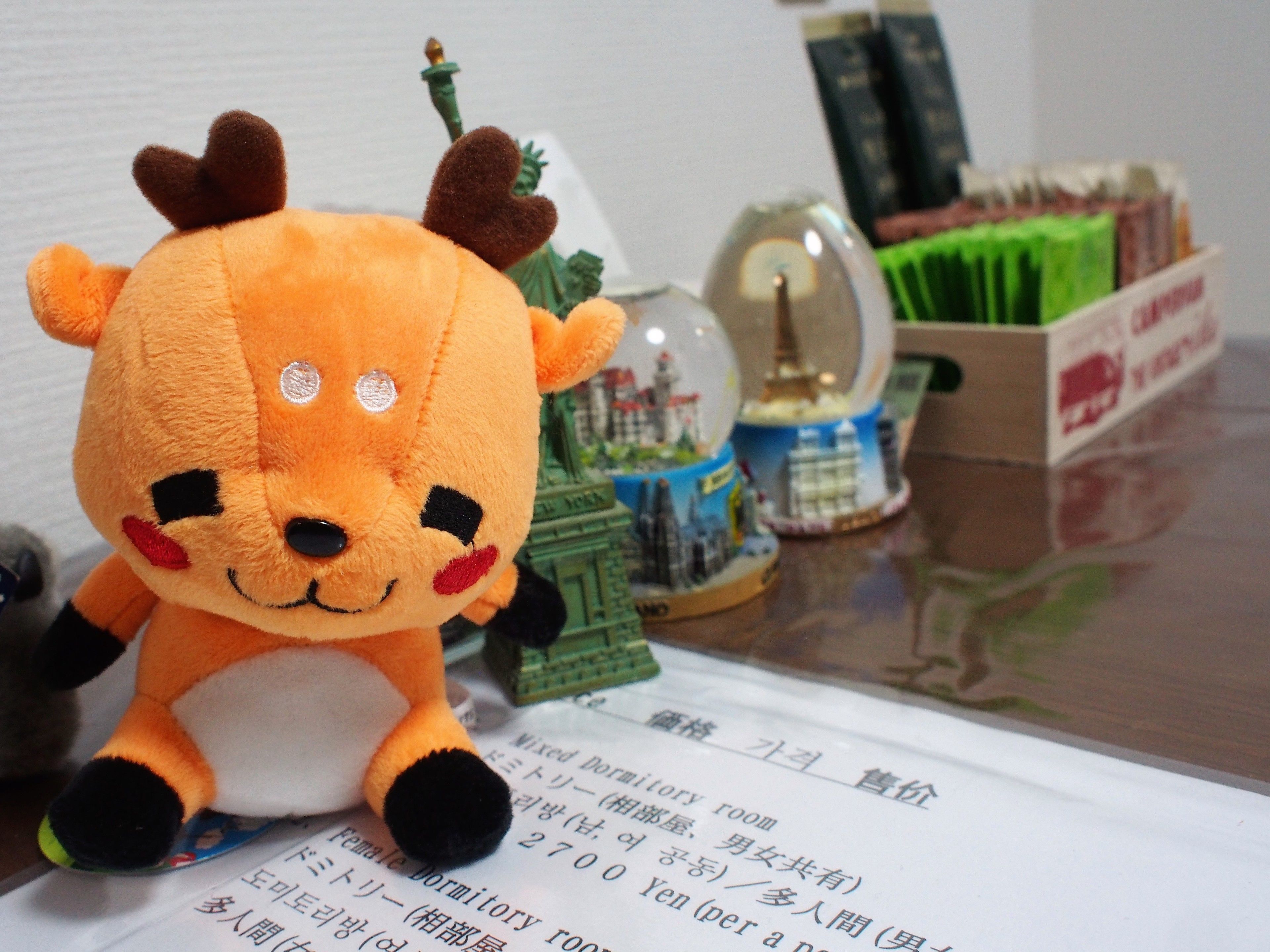 A plush toy on a table with a document, a snow globe, and a green box.