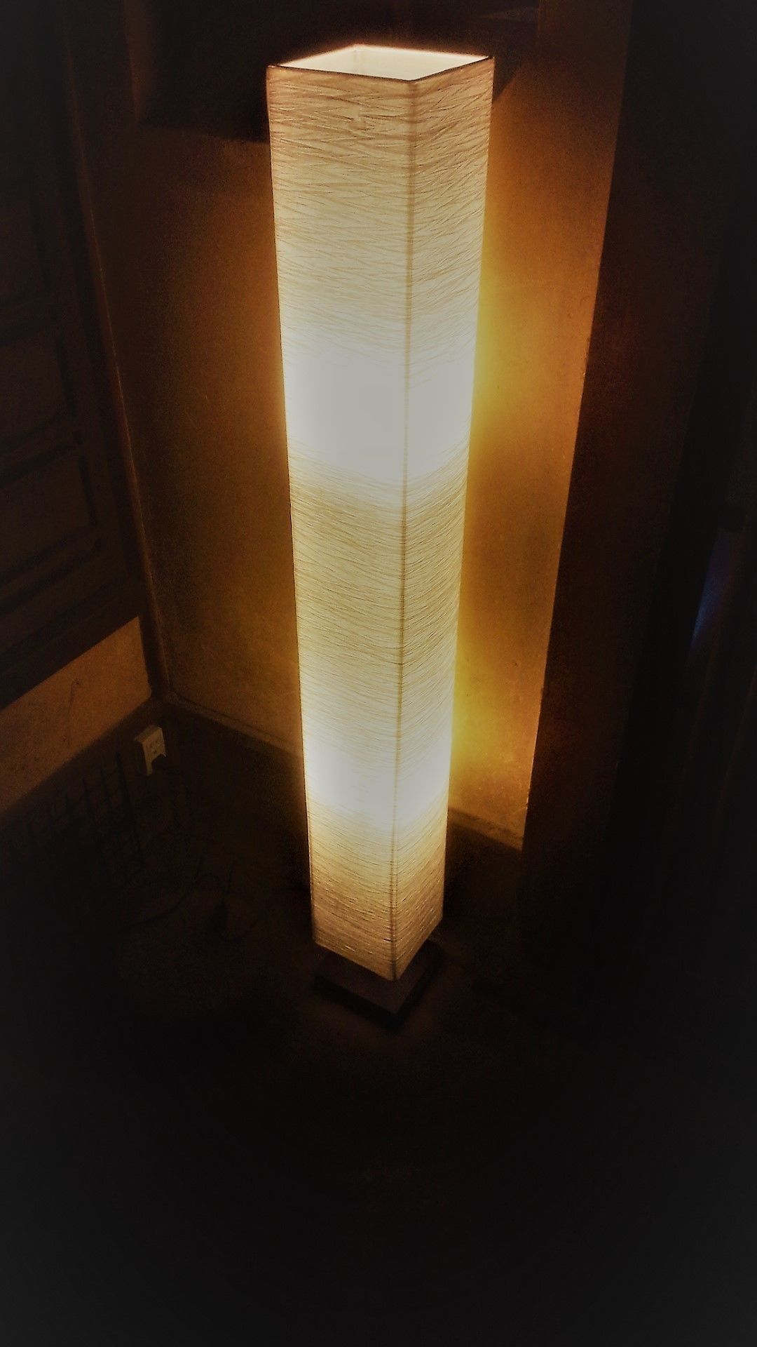 Une lampe haute et étroite, à la texture particulière, qui émet une lumière chaleureuse.