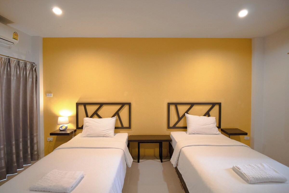 A hotel room with two beds, a nightstand with a lamp, a small table, and a curtain.