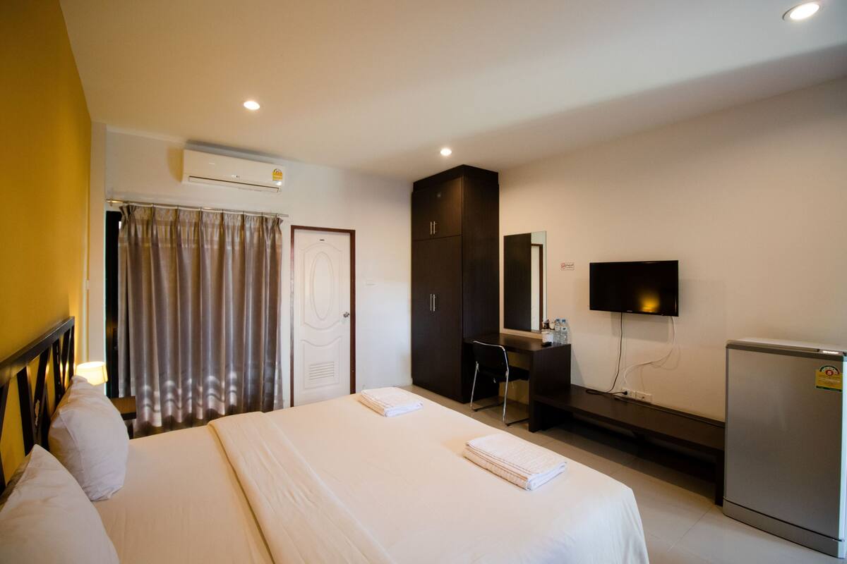 A hotel room with a bed, a desk, a TV, and a refrigerator.