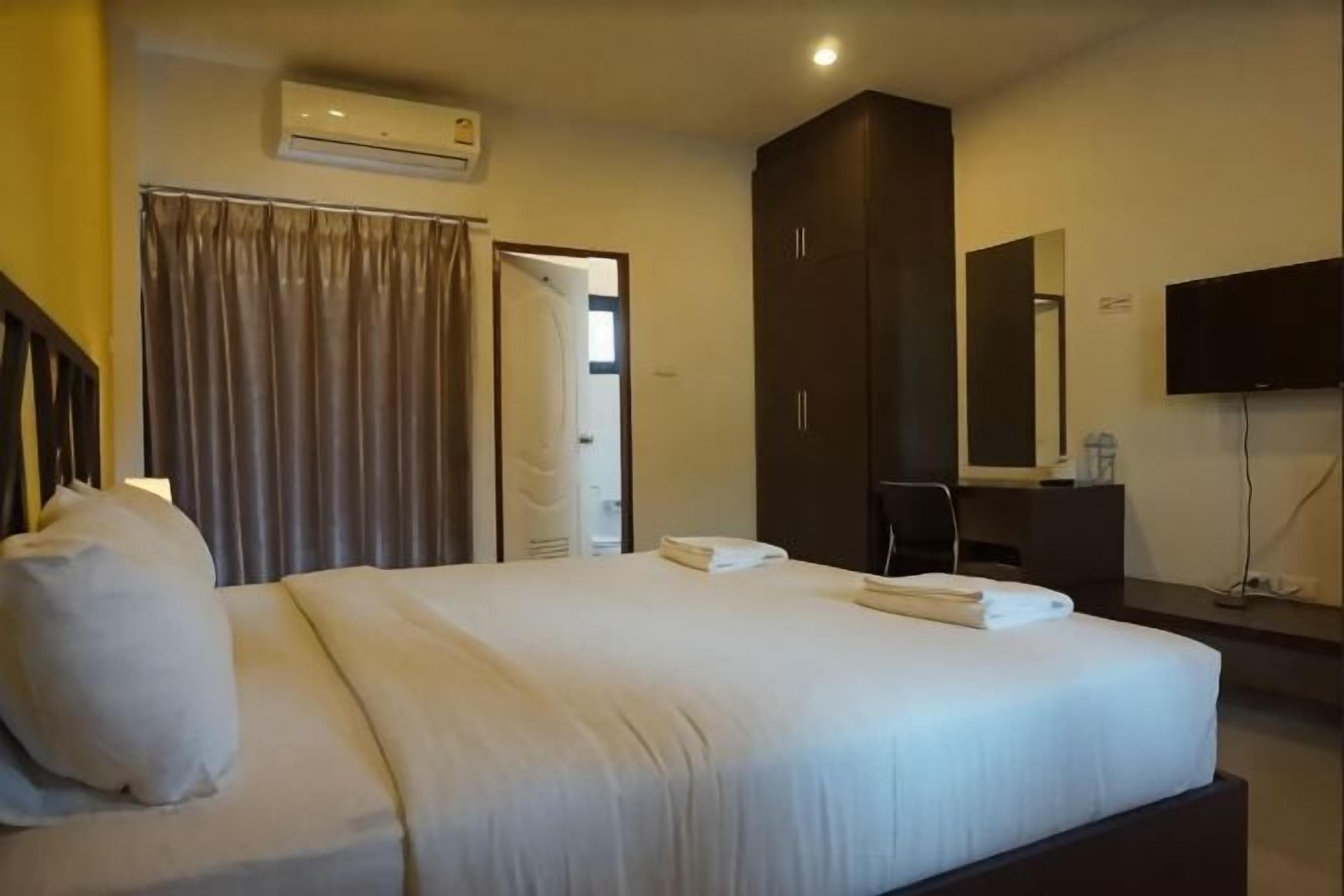A hotel room with a bed, a flat-screen TV, a wardrobe, and an air conditioning unit.