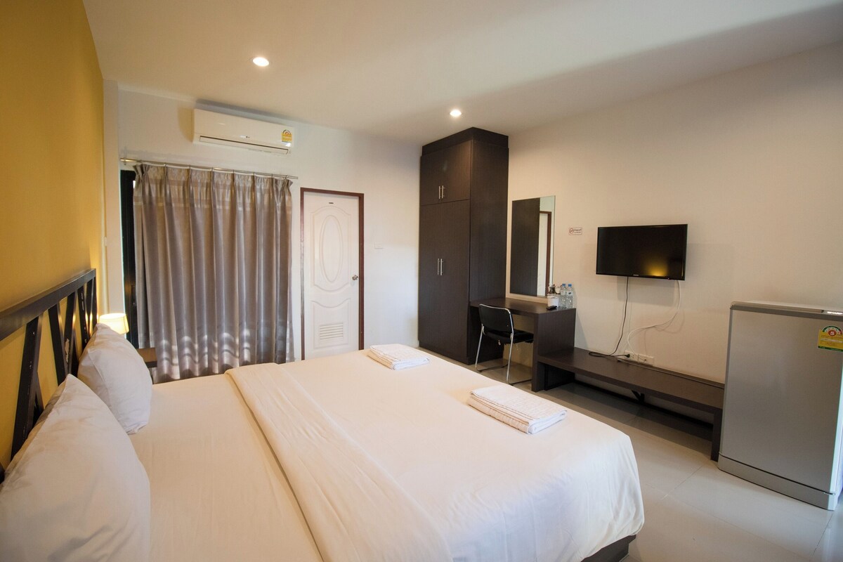 A hotel room with a bed, a desk, a television, and a refrigerator.