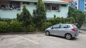 A parking area with a car, a building with balconies, and greenery. - Somsamai Style Apartment (Khon Kaen)