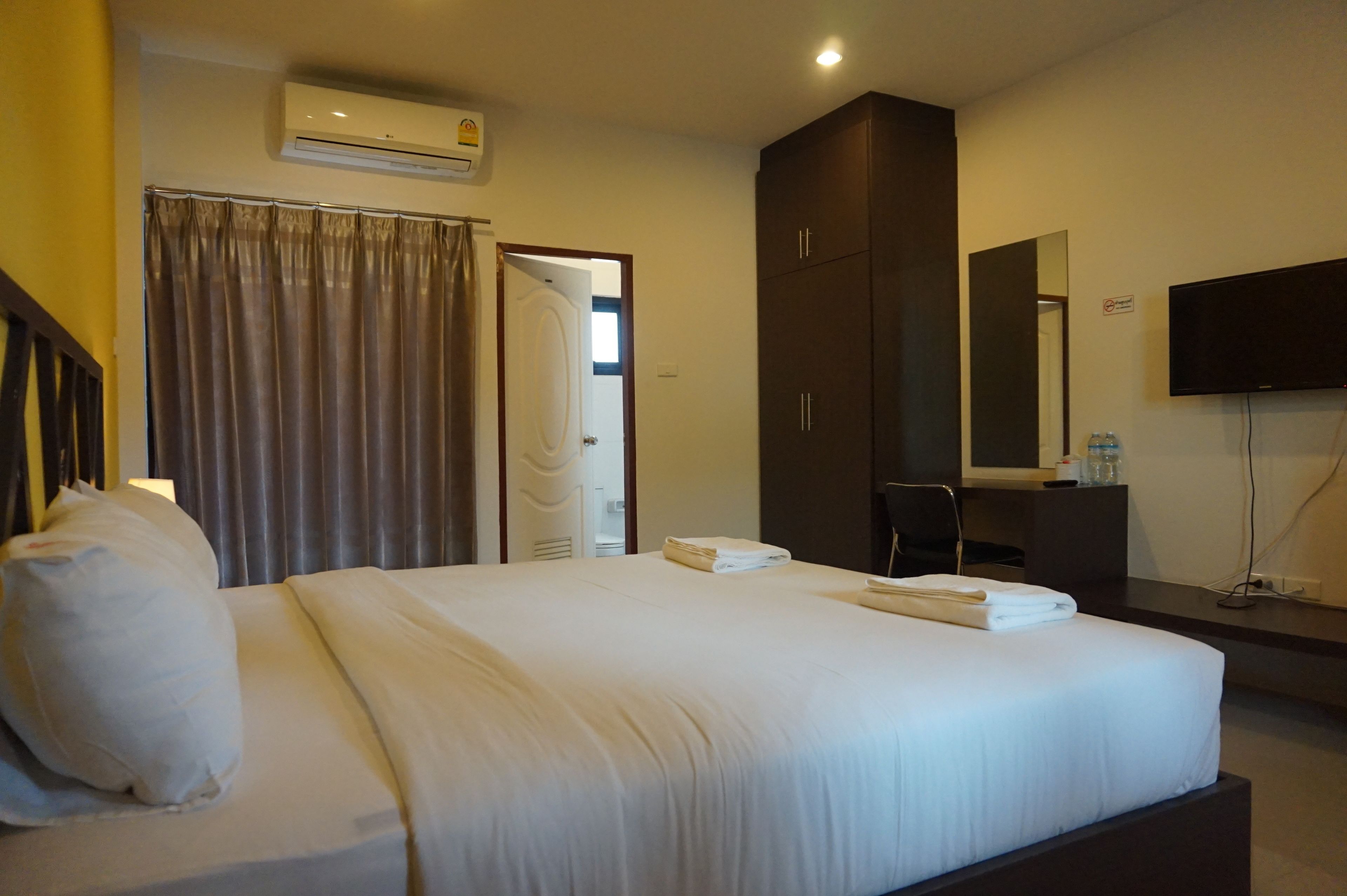 A hotel room with a large bed, a flat-screen TV, a wardrobe, and a bathroom visible through an open door.