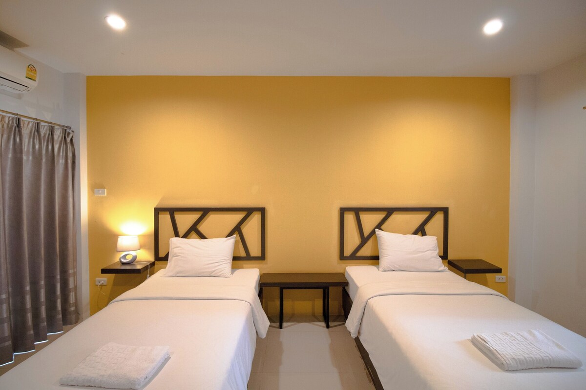 A hotel room with two beds, a nightstand with a lamp, a small table, and a curtain.