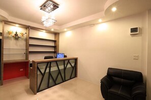 A reception area with a modern desk, a chandelier, and a leather chair.