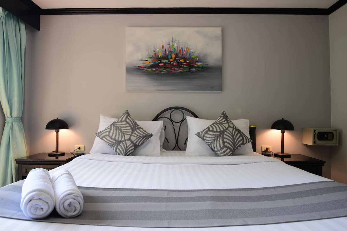 A neatly made bed with striped bedding, two pillows with leaf patterns, and a rolled towel on the side.