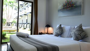Habitación de hotel con cama, mesita de noche, lámpara, un cuadro y vistas al exterior.
