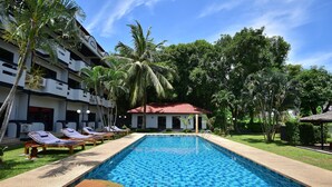 Una piscina con sillas de descanso, palmeras y un edificio con balcones.