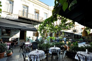 Un café al aire libre con mesas y sillas, rodeado de macetas y cestas colgantes.