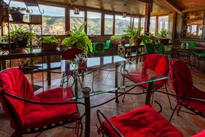 A spacious patio with red chairs and tables, surrounded by potted plants and a view of a valley. - Hotel Penthouse (Tbilisi)