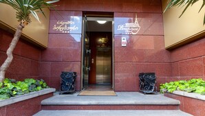 The entrance to a hotel with a red-tiled facade, a palm tree, and decorative ironwork. - Hotel Penthouse (Tbilisi)
