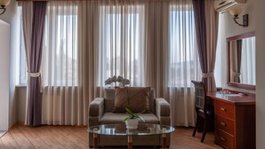 A living room with a sofa, a glass coffee table with a plant, a wooden dresser, and a large window with sheer curtains. - Hotel Penthouse (Tbilisi)