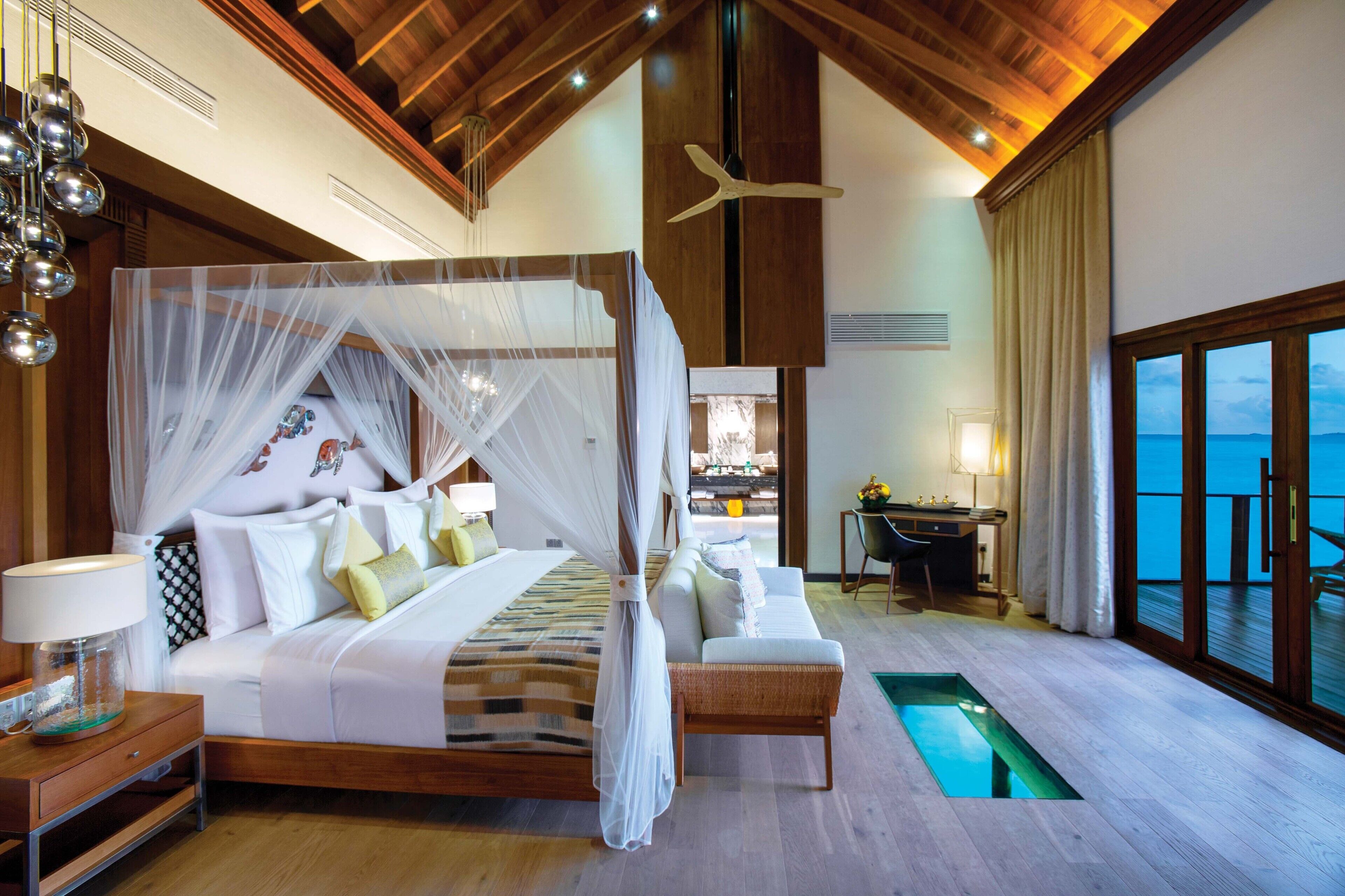 A spacious bedroom with a four-poster bed, a sitting area, and a view of the sea.