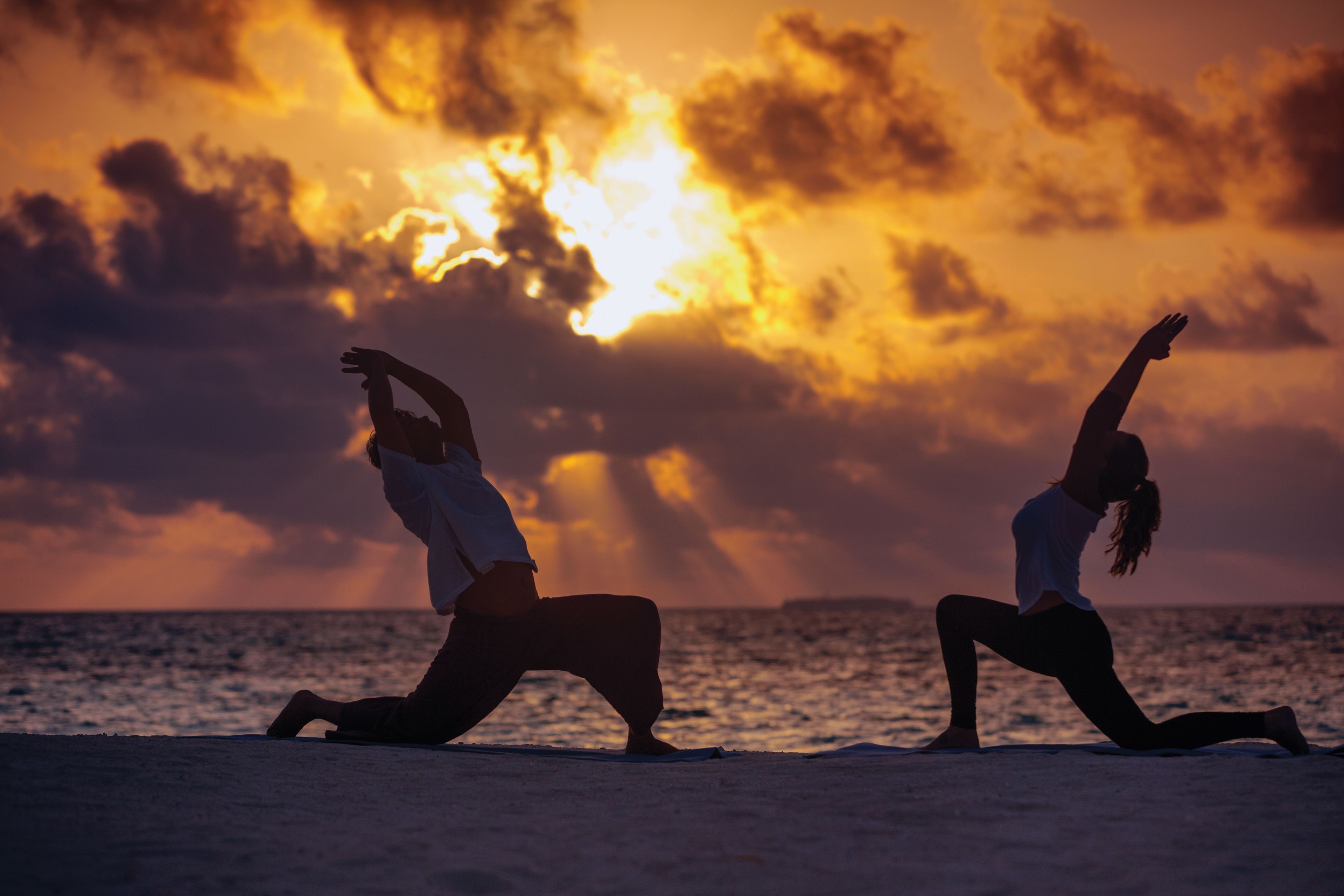Two people performing yoga on a beach with a sunset in the background.