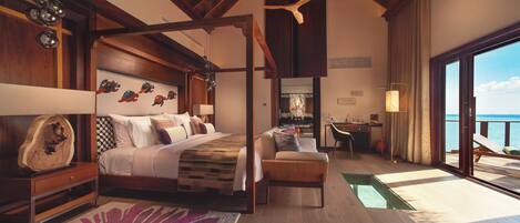 A spacious bedroom with a large bed, a sitting area, and a view of the sea.