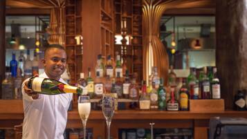 A bar with a bartender pouring a drink into a glass. There are various bottles and glasses on the shelves behind the bartender.