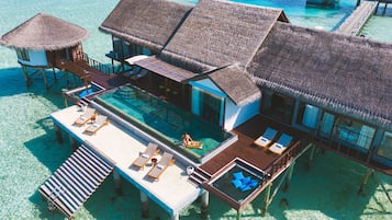 An overwater bungalow with a swimming pool, lounge chairs, and thatched-roof structures.
